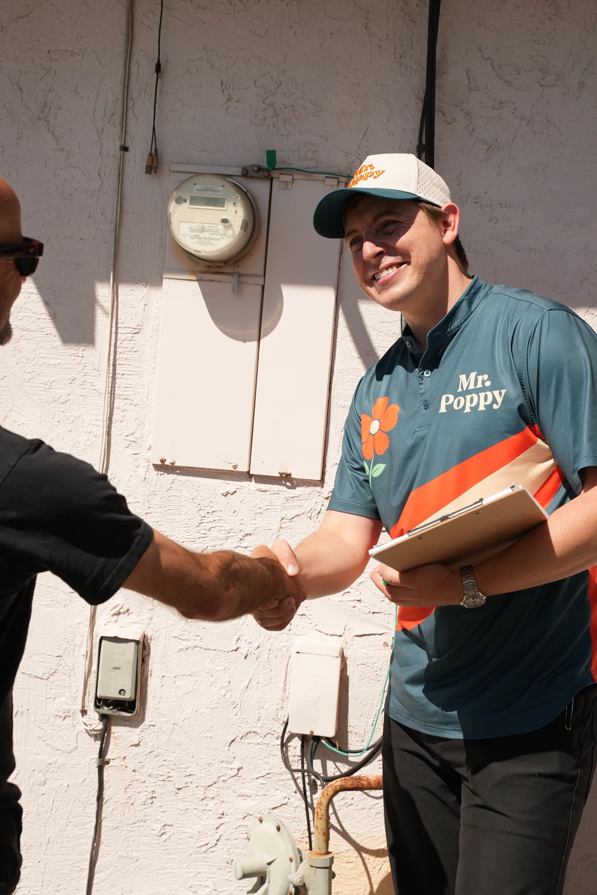 A Mr. Poppy professional shaking hands with a customer beside an outdoor electrical meter.