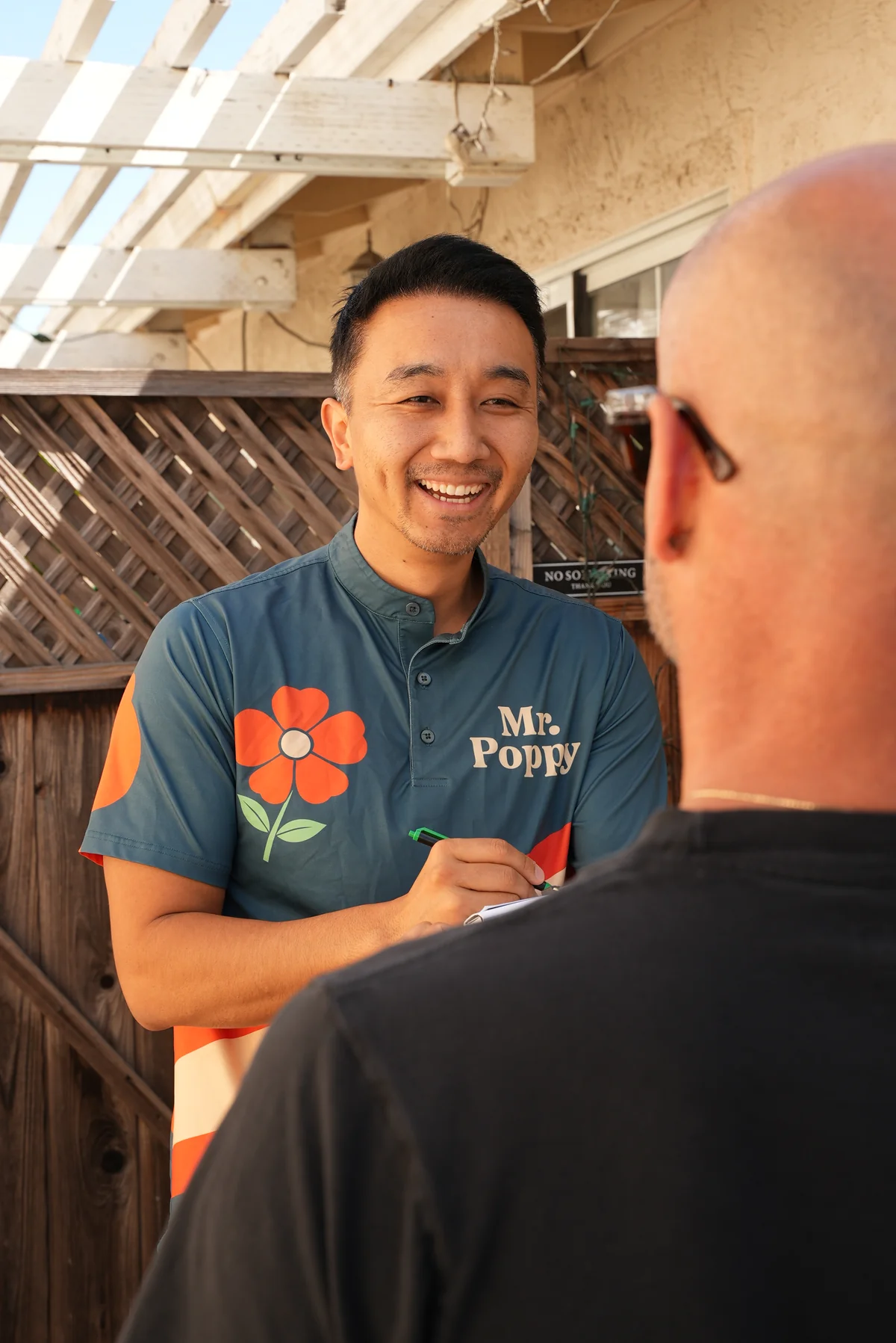 A Mr. Poppy professional holding a clipboard and speaking with a customer outside a home.
